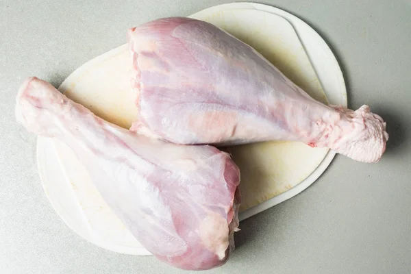 Thawed raw turkey legs on white cutting board for cooking.