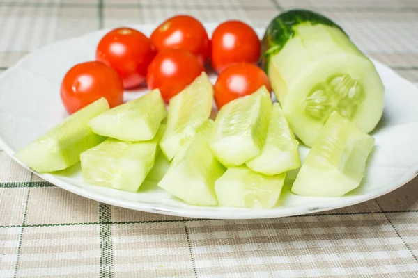 Small red tomatoes and sliced cucumber in plate on kitchen table for snack. — Stock Photo, Image