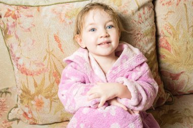 Banyodan sonra ıslak saçlı sevimli bebek kanepede bornozla kurur.