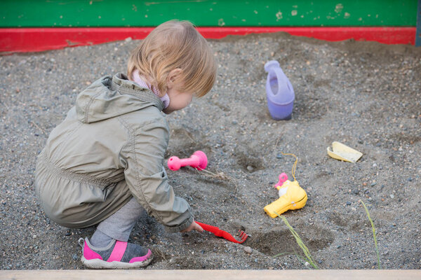 Small child plays with toys in childrens sandbox.