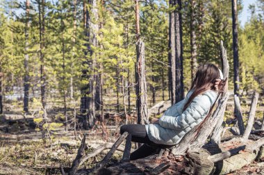 Uzun bir yürüyüşten sonra ceketli yorgun kız çam ormanındaki eski pürüzlerin üzerinde dinleniyor..