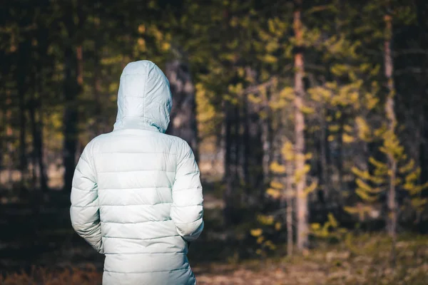 Meisje in lichte jas met capuchon op staat en kijkt kijken naar de diepten van het dennenbos. — Stockfoto