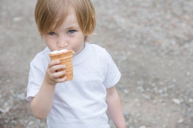 Beyaz tişörtlü, mavi gözlü güzel bebek beyaz dondurma yiyor..
