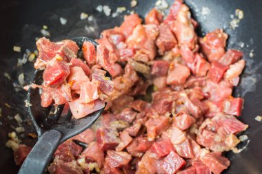 Appetizing pieces of red calf tenderloin with plastic spoon for mixing are fried in large cauldron for pilaf.