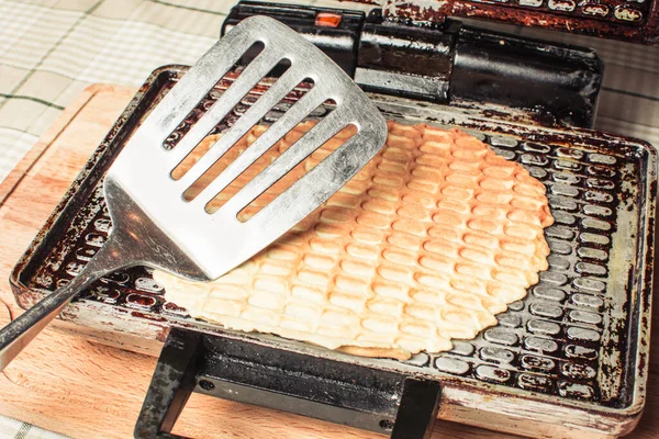 Waffle ızgarasında waffle yaparken mutfak masasını açmak için demir kaşıkla.. — Stok fotoğraf