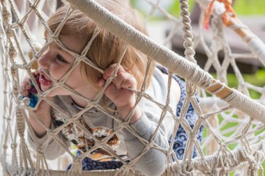 Küçük çocuk oturur ve yüzünü ağlara sıkıştırarak hamakta dinlenir..