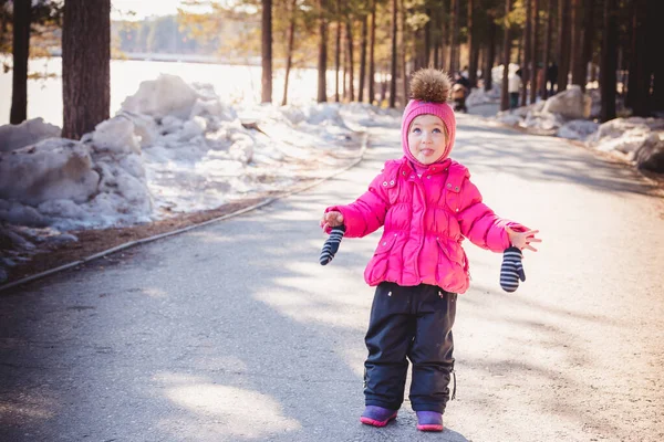冬の服を着た小さな子供が公園を歩き、腕を横に広げ舌を見せる。. — ストック写真