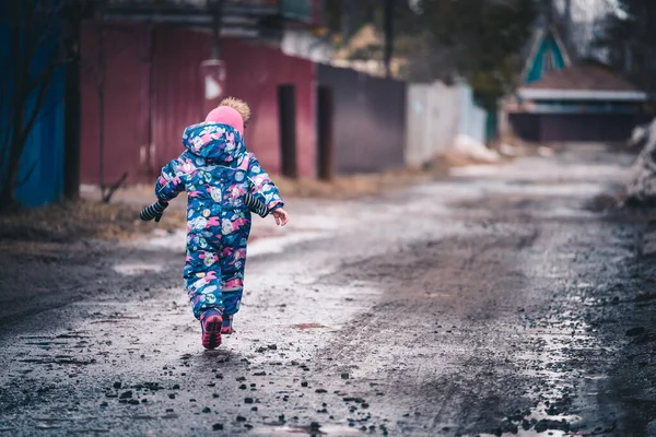 Copil vesel în haine de iarnă merge pe drum în ziua de primăvară . — Fotografie, imagine de stoc