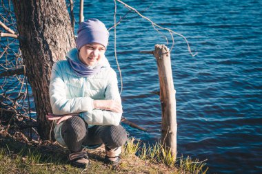 Ceketli ve şapkalı güzel bir kız bahar günü gölün kıyısında oturur.