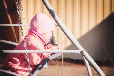 Ceketli ve şapkalı küçük çocuk güneşli bir günde salıncakta sallanıyor.