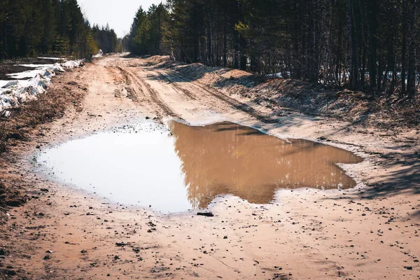 Deep spring puddle on the sandy road due to melting snow after winter