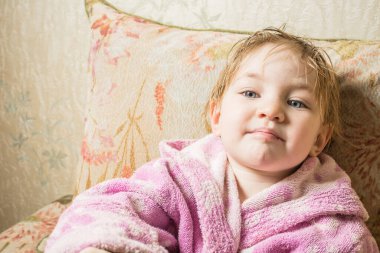 Banyodan sonra ıslak saçlı sevimli bebek kanepede bornozla kurur