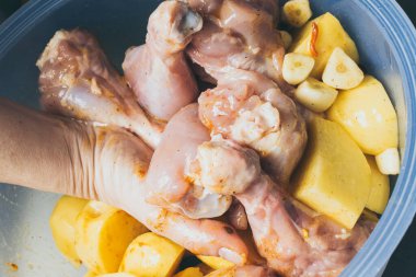 Dişi el tavuk bacaklarını fırında pişirmek için patatesle marine ediyor.