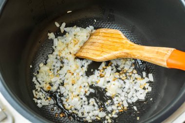 Tahta kaşıkla dilimlenmiş soğan, yemek pişirmek için tencerede kızartılır.