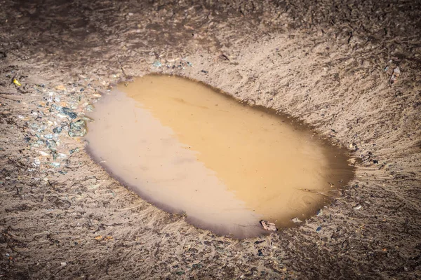 Deep spring puddle on the sandy road due to melting snow after winter