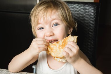 Mavi gözlü güzel bebek, mutfak masasında sandalyede otururken lezzetli krepler yiyor.