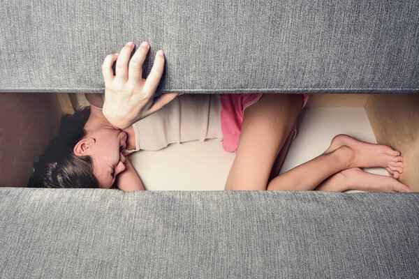 Девушка с открытым ртом, прячущаяся в диване, закрывает его. Понятие жестокого обращения с детьми
