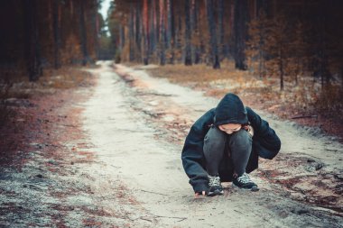 Kapüşonlu yetişkin bir kız ormanda kumla oynuyor.