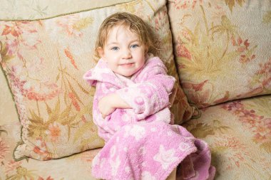 Banyodan sonra ıslak saçlı sevimli bebek kanepede bornozla kurur