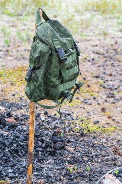 Haki yürüyüşü için bir sırt çantası. Yaz ormanlarında yanan kömürün arka planında ince bir tahta çubukta asılı duruyor.