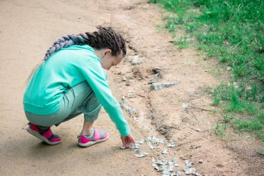 Kafasında rastalı bir kız yerde bir grup beyaz kelebekle oynuyor.