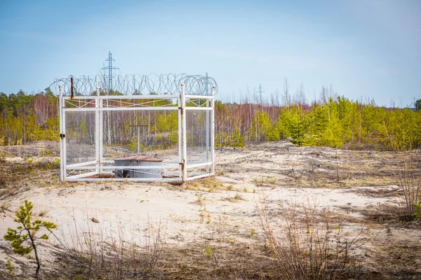 Fenced oil compressor with an iron fence and barbed wire mounted on the sand outside the city in flattering area