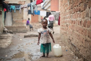 KAMPALA, UGANDA, JANUARY 26, 2020: Bilinmeyen bir kız teneke kutuyla annesine Katanga gecekondu mahallesinde yardım etmeye gider, Kampala, Uganda. Gecekondudaki çocuklar okula başlamadan önce ödevlerine yardım etmeye başlarlar..