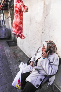 Kahire, Mısır Bir kadın telefonda konuşurken asılı bir domuzun yanında oturuyor.