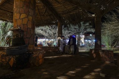 Siwa Oasis, Mısır, Parkta geceleyin palmiye ağacının altında oturan adamlar.