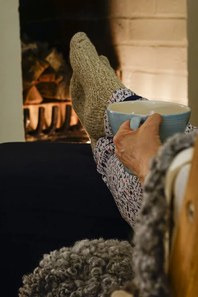 Stockholm, Sweden A couple sit together drinking tea with wool socks in front of fireplace.