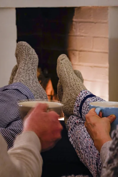 Stockholm, Sweden A couple sit together drinking tea with wool socks in front of fireplace.