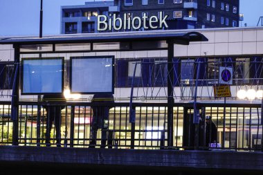 Stockholm, İsveç insanlar Hogdalen 'de bir otobüs durağında ve halk kütüphanesi için bir tabela bekliyor..