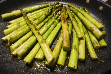 Taze yeşil kuşkonmaz, zeytinyağlı tavada kızartılıyor.