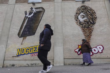 Flen, İsveçli Müslüman göçmen kadınlar büyük cam dondurma fabrikasına ait dondurma figürleriyle duvarın önünden yürüyorlar..