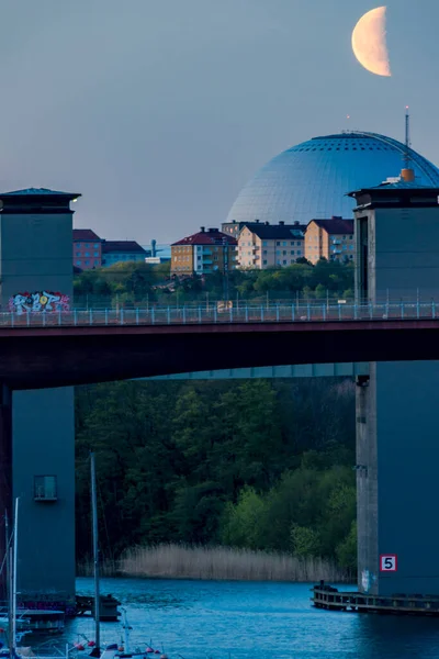 Stockholm, Sweden  The Ercisson Globe Arena at night with a half moon rising over the Arsta train bridge.