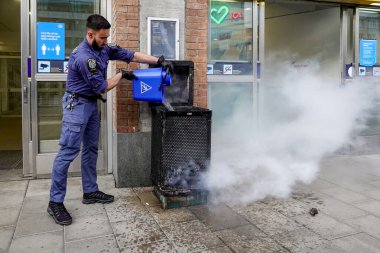 Stockholm, İsveç 16 Mayıs 2020. Bir güvenlik görevlisi, Hornstull metrosunun girişindeki yanan bir çöp tenekesini ya da tünel istasyonunu bir kova suyla söndürdü..