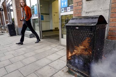 Stockholm, İsveç 16 Mayıs 2020 Hornstull metro veya tünelbana istasyonunun girişinde yanan bir çöp tenekesinin yanından geçen bir yaya..