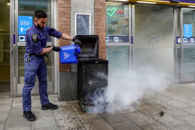 Stockholm, İsveç 16 Mayıs 2020. Bir güvenlik görevlisi, Hornstull metrosunun girişindeki yanan bir çöp tenekesini ya da tünel istasyonunu bir kova suyla söndürdü..