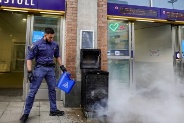 Stockholm, İsveç 16 Mayıs 2020. Bir güvenlik görevlisi, Hornstull metrosunun girişindeki yanan bir çöp tenekesini ya da tünel istasyonunu bir kova suyla söndürdü..