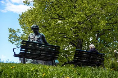 Stockholm, Sweden A man sits on a bench in the Tegnerlunden park next to the August Strindberg statue by Carl Eldh.