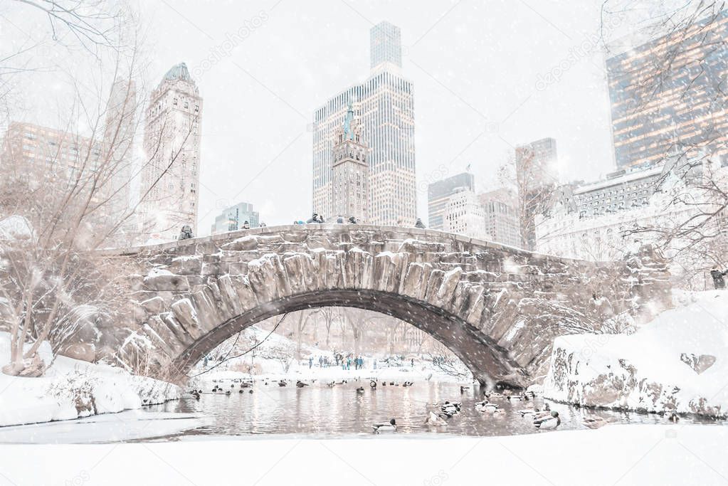 Central Park snow covered Gapstow Bridge in the winter with the NYC cityscape peaking in the background