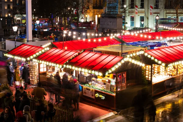 Londres, Reino Unido / Europa; 20 / 12 / 2019: Vista noturna do mercado de Natal na Trafalgar Square. Longa exposição tiro com pessoas enterradas andando e fazendo compras . — Fotografia de Stock