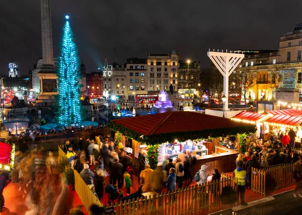 London, uk / europa; 20 / 12 / 2019: nachtansicht weihnachtsmarkt, weihnachtsbaum und menora in trafalgar square in london. Langzeitbelichtungsaufnahmen mit verschwommenen Menschen beim Spazierengehen und Einkaufen. — Stockfoto