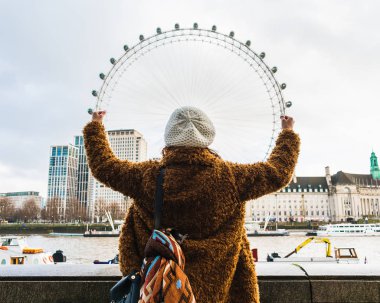 Sırtında Londra 'nın en ünlü simgelerinden biri olan London Eye' ı tutan genç bir kadın.