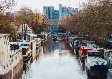 Londra 'nın Little Venice bölgesindeki bir kanalda park halindeki yüzen evler arasında giden tekne.