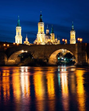 İspanya 'nın Zaragoza kentindeki mavi saat boyunca Basilica del Pilar ve Puente de Piedra Ebro nehrine yansıdı.
