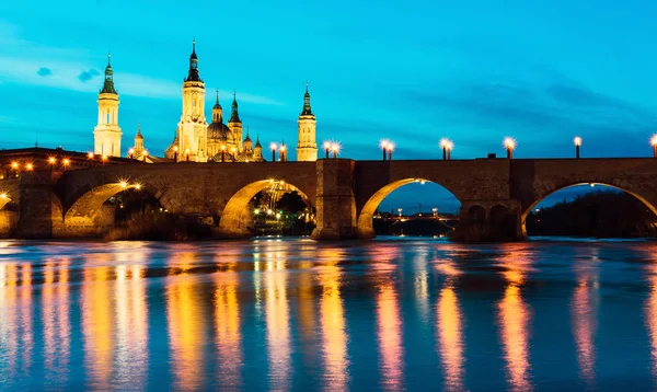 İspanya 'nın Zaragoza kentindeki mavi saat boyunca Basilica del Pilar ve Puente de Piedra Ebro nehrine yansıdı.