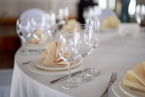 Cutlery on the table, clear glass champagne glasses, white tableware plate with beige peach napkin, knife and fork, table without people, clean tableware without food