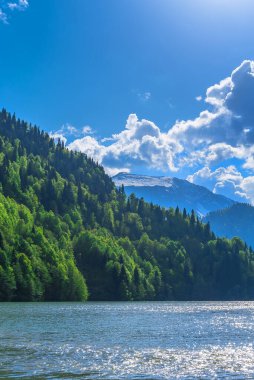 Kafkas Dağları 'ndaki güzel Ritsa Gölü. Yeşil dağ tepeleri, bulutlu mavi gökyüzü. Bahar manzarası