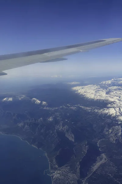 Winter mountains from the plane window with plane wing. Turkish mountains landscape aerial view. Snow peaks